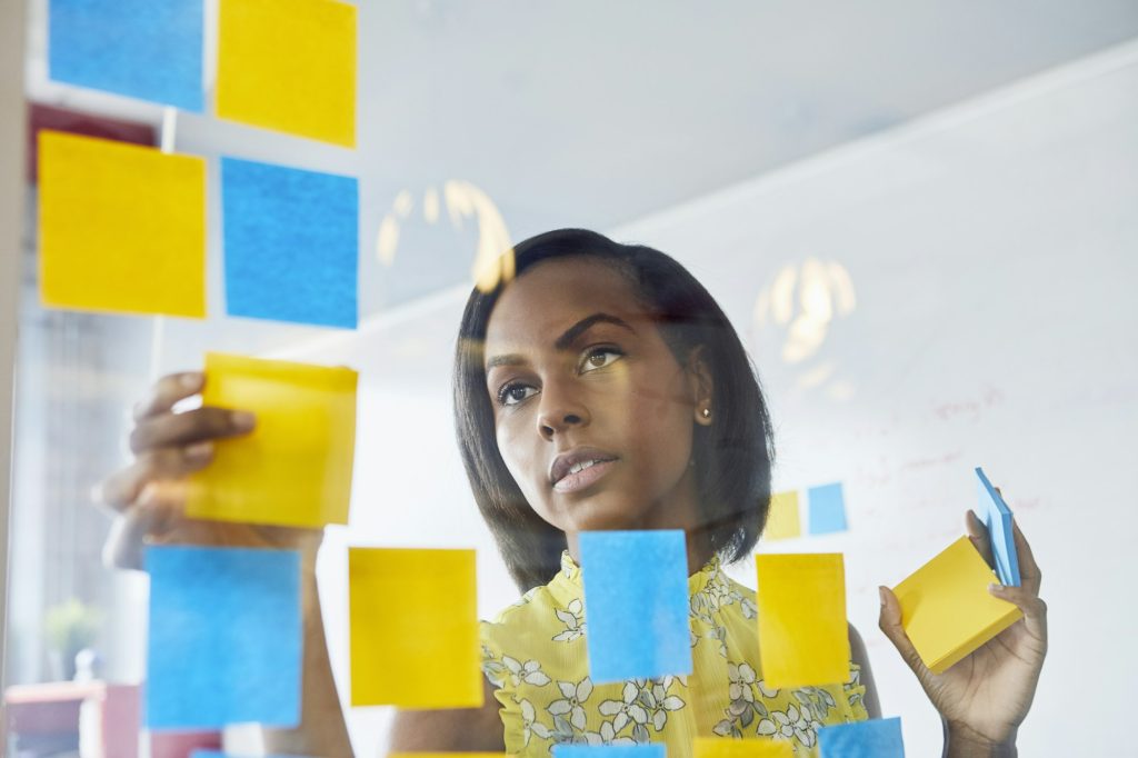 Young woman in office, sticking sticky notes to glass in office